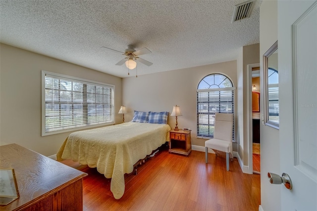 bedroom featuring a textured ceiling, ceiling fan, wood finished floors, visible vents, and baseboards