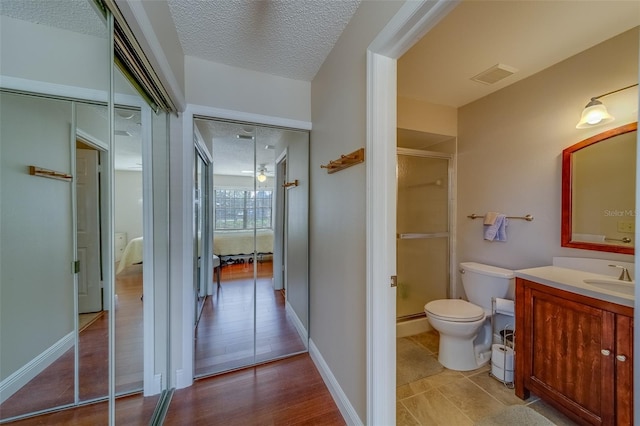 bathroom featuring a textured ceiling, toilet, vanity, visible vents, and a shower stall