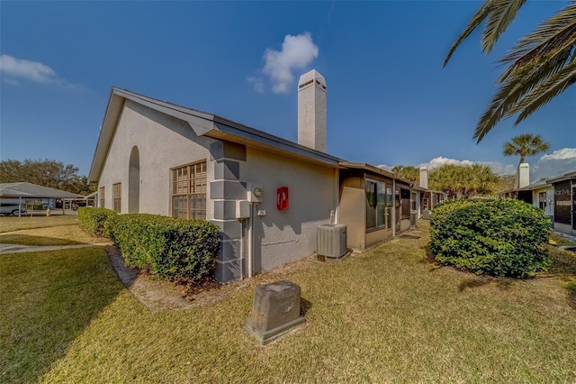 view of property exterior with a chimney, a lawn, stucco siding, and central air condition unit