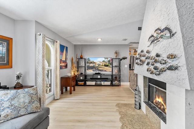 living room with lofted ceiling, a textured ceiling, a fireplace, and light hardwood / wood-style floors