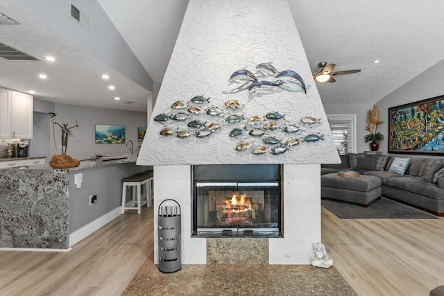 living room with lofted ceiling, a large fireplace, and light wood-type flooring