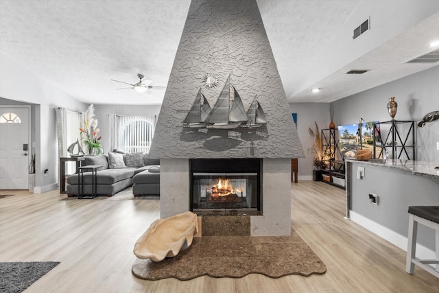 living room featuring ceiling fan, a multi sided fireplace, a textured ceiling, and light wood-type flooring