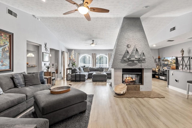 living room with ceiling fan, a multi sided fireplace, light hardwood / wood-style flooring, and a textured ceiling