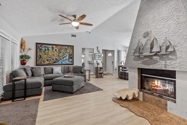 living room featuring lofted ceiling, a textured ceiling, a wealth of natural light, a high end fireplace, and light hardwood / wood-style floors