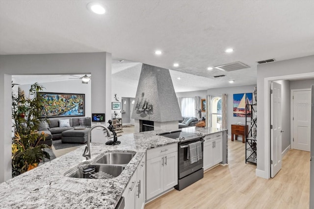 kitchen with sink, light hardwood / wood-style flooring, stainless steel range with electric stovetop, light stone countertops, and white cabinets