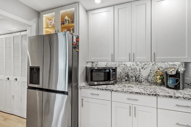 kitchen with white cabinetry, light wood-type flooring, appliances with stainless steel finishes, light stone countertops, and decorative backsplash