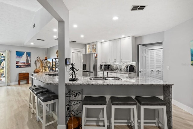 kitchen featuring light stone counters, light hardwood / wood-style flooring, appliances with stainless steel finishes, a kitchen breakfast bar, and white cabinets