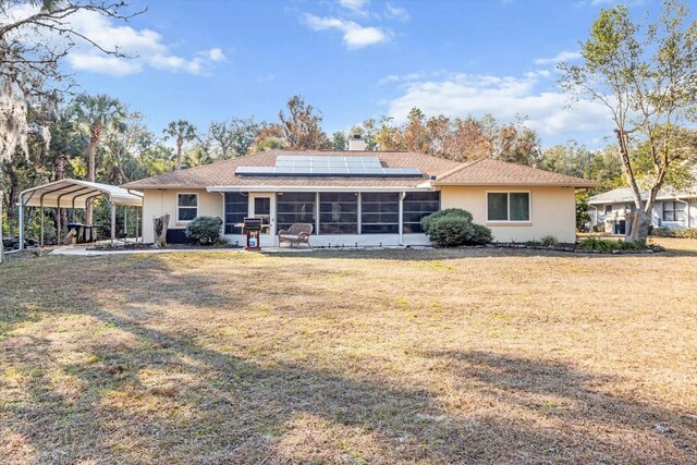 back of house with a carport, a sunroom, a yard, and solar panels