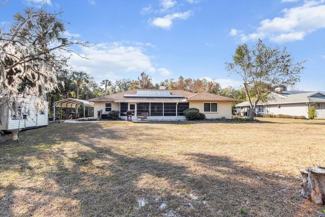 back of property featuring a lawn, a sunroom, a carport, and solar panels