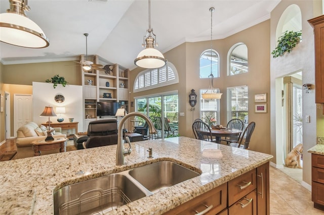 kitchen with sink, crown molding, light tile patterned floors, pendant lighting, and light stone countertops