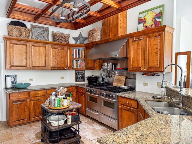 kitchen featuring double oven range, light stone countertops, sink, and wall chimney range hood