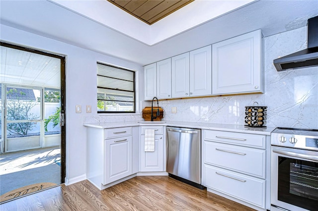 kitchen featuring white cabinetry, appliances with stainless steel finishes, light hardwood / wood-style floors, and wall chimney range hood