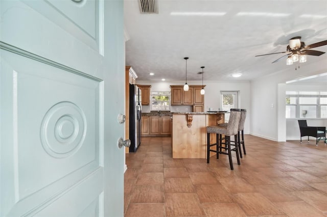 kitchen featuring hanging light fixtures, stainless steel fridge, a kitchen breakfast bar, a kitchen island, and stone counters