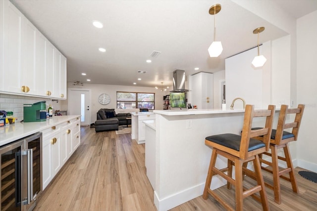 kitchen featuring a breakfast bar area, white cabinetry, island range hood, decorative light fixtures, and beverage cooler