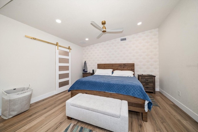 bedroom with ceiling fan, wood-type flooring, and a barn door