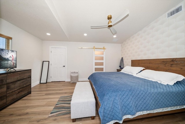 bedroom with light hardwood / wood-style flooring, a barn door, and ceiling fan