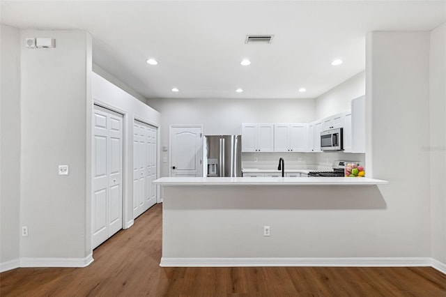 kitchen with wood-type flooring, sink, white cabinets, kitchen peninsula, and stainless steel appliances