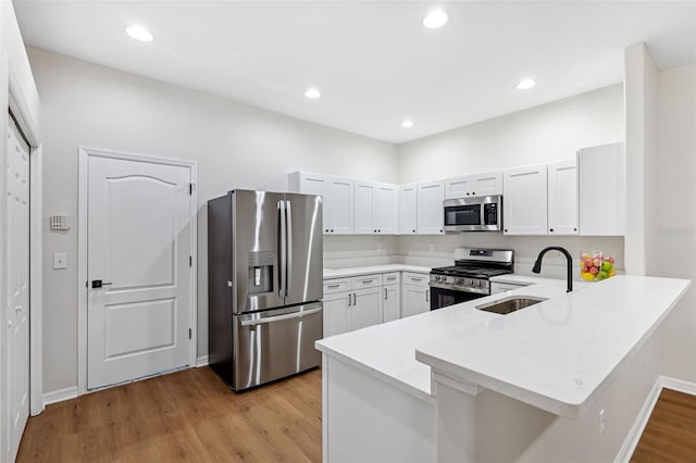 kitchen featuring appliances with stainless steel finishes, white cabinetry, sink, light hardwood / wood-style floors, and kitchen peninsula