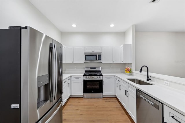 kitchen featuring appliances with stainless steel finishes, sink, white cabinets, kitchen peninsula, and light wood-type flooring