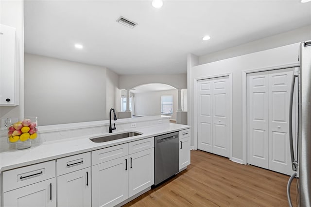 kitchen featuring sink, appliances with stainless steel finishes, light stone countertops, light hardwood / wood-style floors, and white cabinets