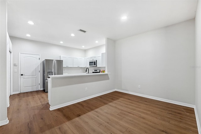 kitchen featuring stainless steel appliances, hardwood / wood-style flooring, white cabinets, and kitchen peninsula