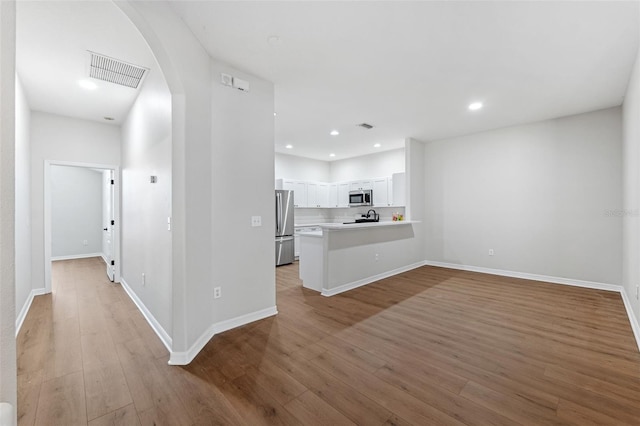 kitchen featuring stainless steel appliances, white cabinetry, light wood-type flooring, and kitchen peninsula