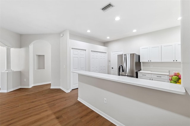 kitchen with stainless steel fridge with ice dispenser, decorative columns, white cabinetry, wood-type flooring, and kitchen peninsula