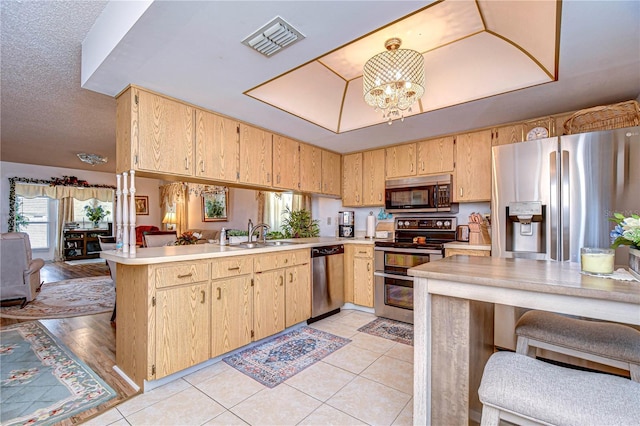 kitchen with sink, an inviting chandelier, light brown cabinets, appliances with stainless steel finishes, and kitchen peninsula