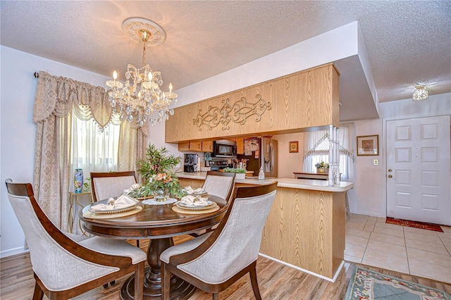 dining room with light wood-type flooring, a notable chandelier, and a textured ceiling