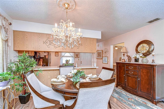 dining area featuring a textured ceiling, a notable chandelier, and light wood-type flooring