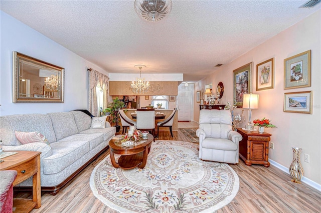 living room featuring an inviting chandelier, a textured ceiling, and light hardwood / wood-style floors