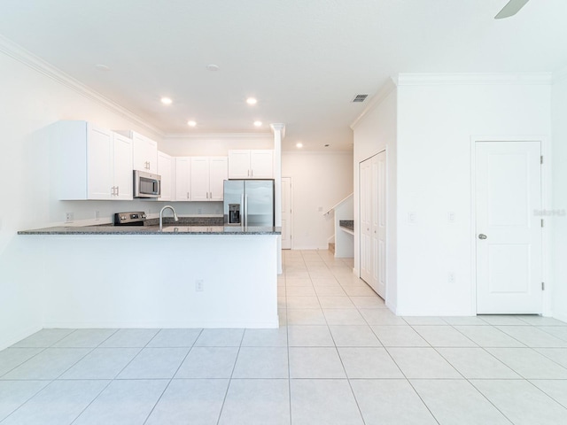 kitchen with appliances with stainless steel finishes, white cabinetry, ornamental molding, kitchen peninsula, and dark stone counters