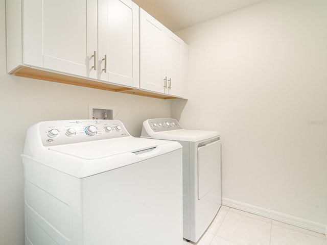 washroom with light tile patterned flooring, cabinets, and washing machine and clothes dryer