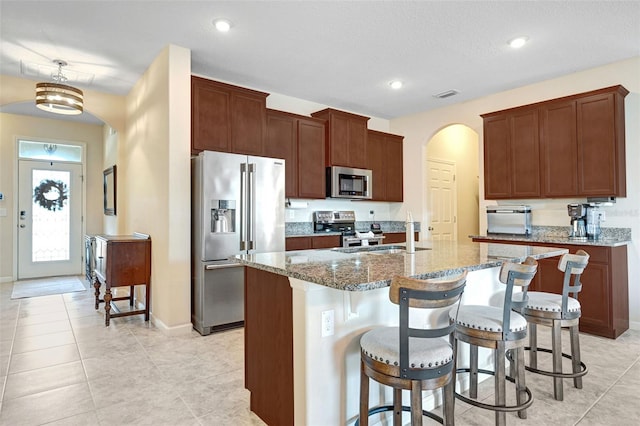 kitchen with sink, light stone counters, pendant lighting, stainless steel appliances, and a kitchen island with sink