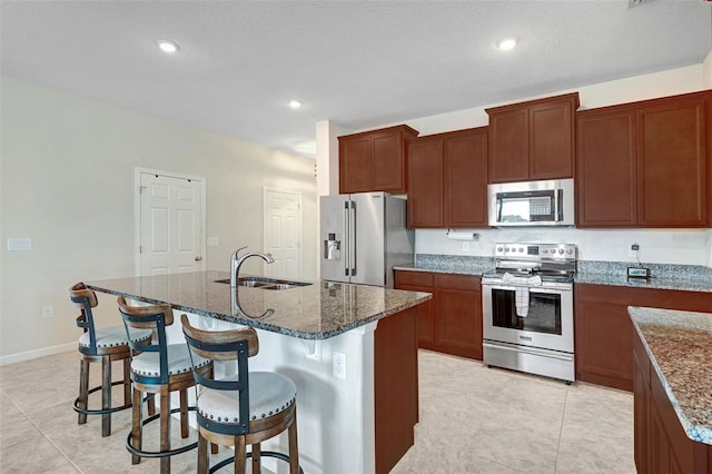 kitchen with sink, a breakfast bar area, dark stone countertops, appliances with stainless steel finishes, and an island with sink