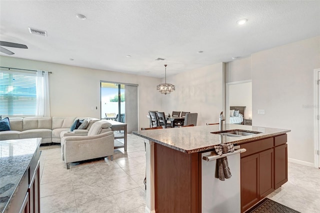 kitchen featuring an island with sink, stainless steel dishwasher, a wealth of natural light, and decorative light fixtures