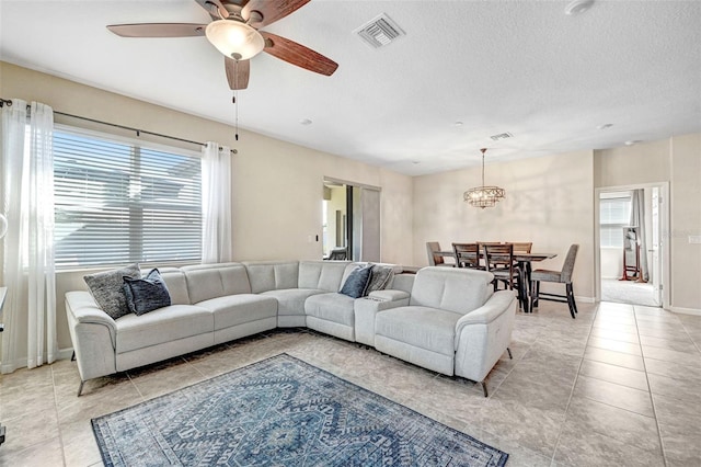 living room with light tile patterned flooring, ceiling fan with notable chandelier, and a textured ceiling