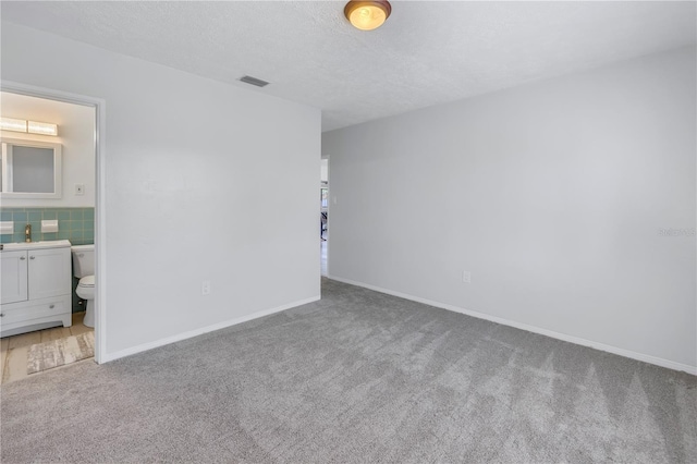 unfurnished bedroom featuring ensuite bathroom, light colored carpet, and a textured ceiling