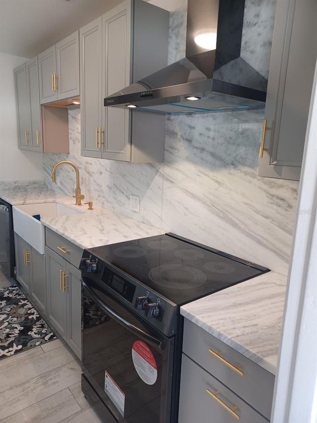 kitchen with gray cabinets, wall chimney range hood, and black appliances