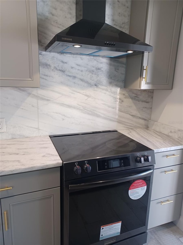 kitchen featuring black electric range oven, gray cabinets, backsplash, light stone counters, and wall chimney exhaust hood