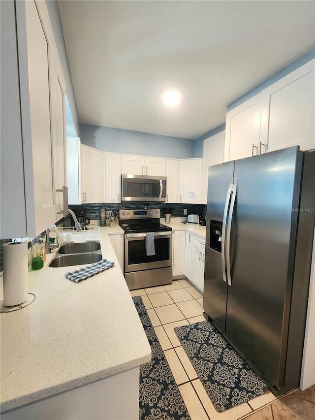 kitchen featuring tasteful backsplash, light tile patterned floors, a sink, appliances with stainless steel finishes, and white cabinetry