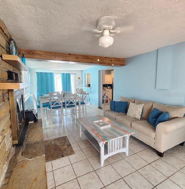 living area featuring a stone fireplace, light tile patterned floors, a textured ceiling, a ceiling fan, and beam ceiling