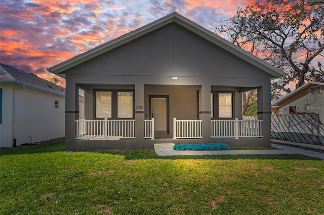 back house at dusk featuring a porch and a lawn