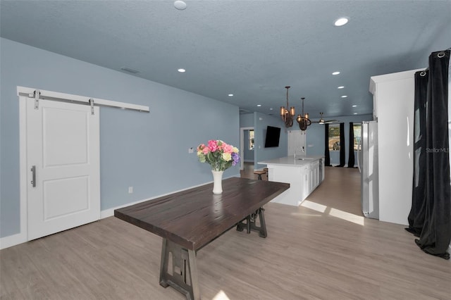 dining room with sink, an inviting chandelier, a textured ceiling, a barn door, and light wood-type flooring