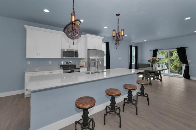 kitchen featuring pendant lighting, sink, appliances with stainless steel finishes, white cabinetry, and a kitchen island with sink