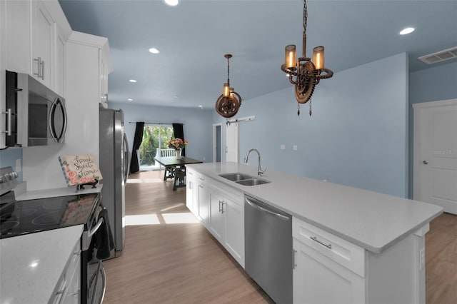 kitchen featuring pendant lighting, white cabinetry, sink, stainless steel appliances, and light hardwood / wood-style flooring