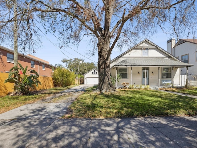 bungalow-style house with a front yard, a garage, a porch, and an outbuilding