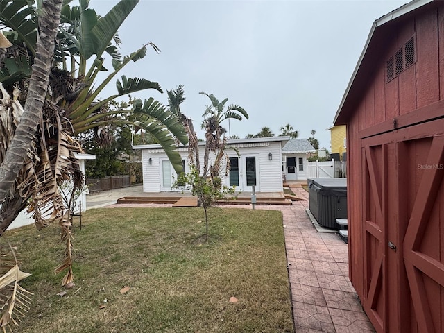 back of house with an outbuilding, a hot tub, a patio area, and a lawn