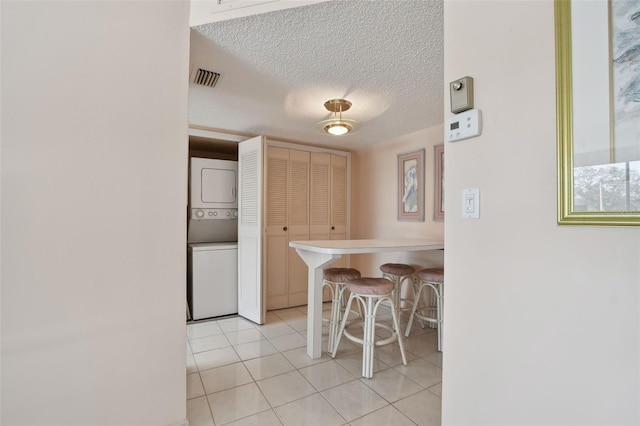 kitchen featuring light tile patterned floors, a breakfast bar, stacked washer and clothes dryer, a textured ceiling, and kitchen peninsula