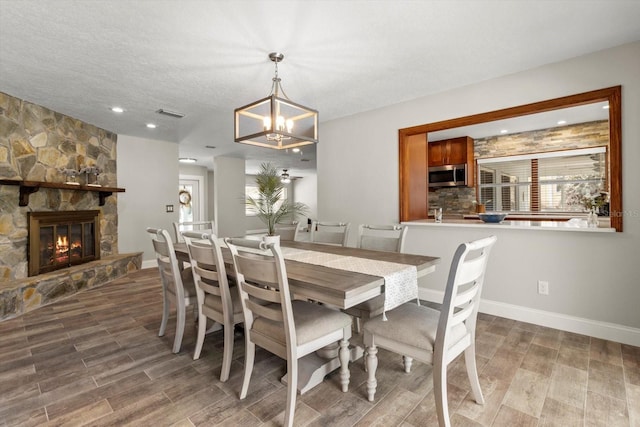 dining room featuring an inviting chandelier, wood-type flooring, a stone fireplace, and a textured ceiling